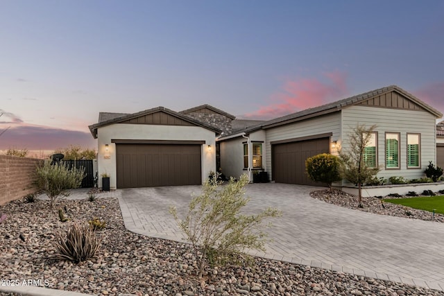 view of front of property with an attached garage, board and batten siding, fence, and decorative driveway