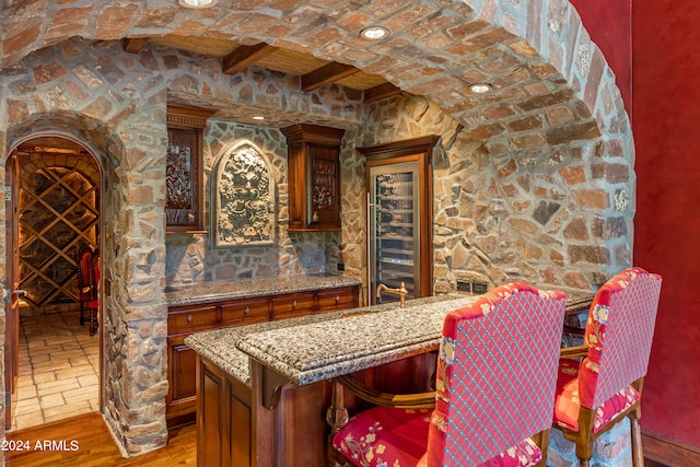 bar with beam ceiling, light stone counters, and hardwood / wood-style flooring