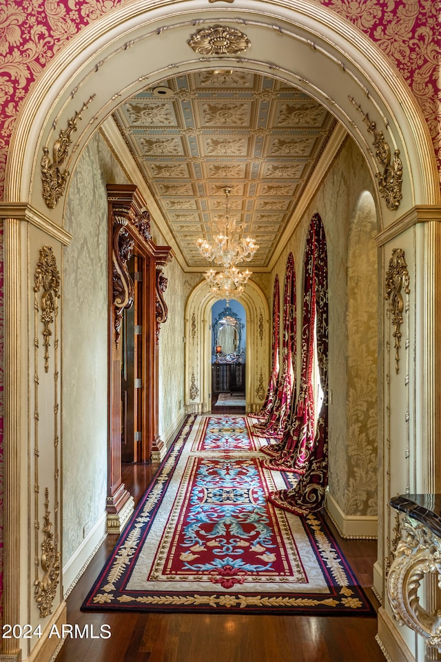 hall featuring decorative columns, ornamental molding, dark wood-type flooring, and a chandelier