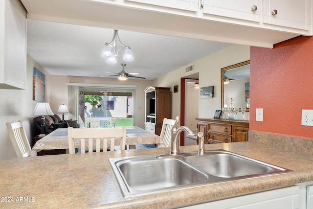 kitchen with hanging light fixtures, white cabinets, ceiling fan with notable chandelier, a textured ceiling, and sink