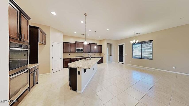 kitchen with an island with sink, sink, hanging light fixtures, light stone counters, and stainless steel appliances