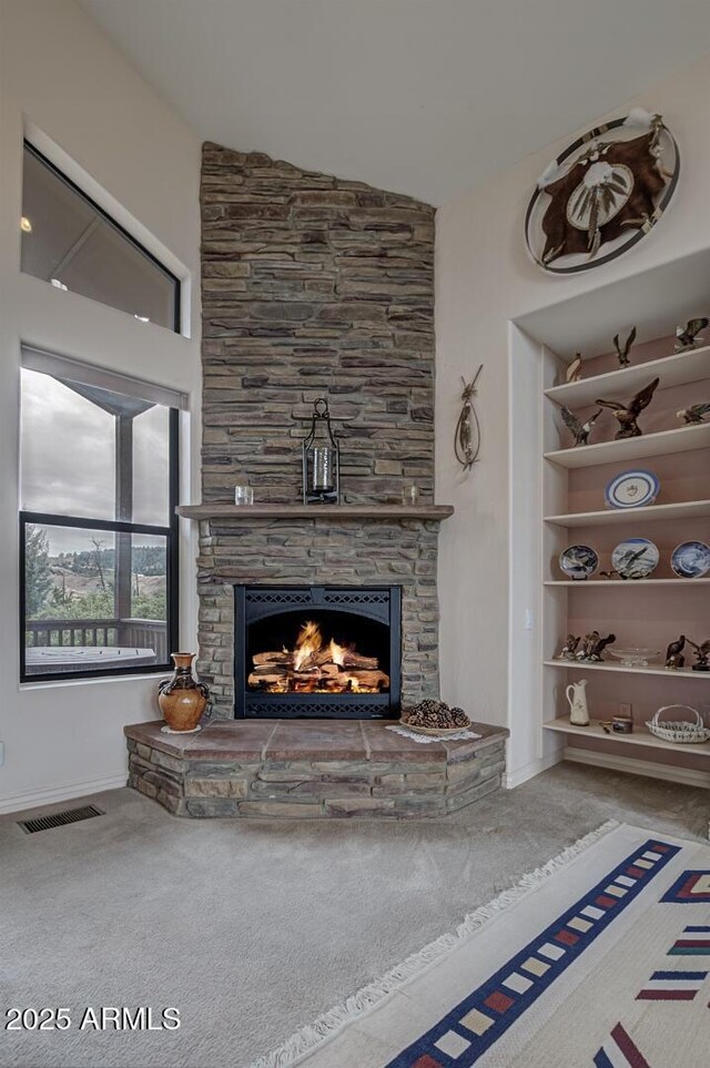 carpeted living room with visible vents and a stone fireplace