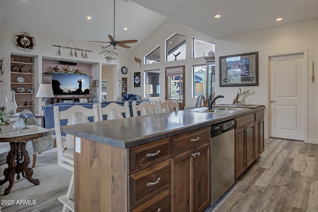 kitchen with dark countertops, a kitchen island with sink, dishwasher, and a sink