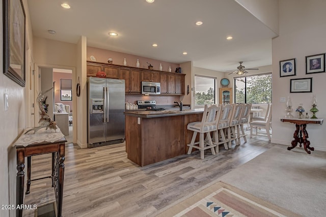 kitchen with recessed lighting, appliances with stainless steel finishes, light wood-style floors, an island with sink, and a kitchen bar