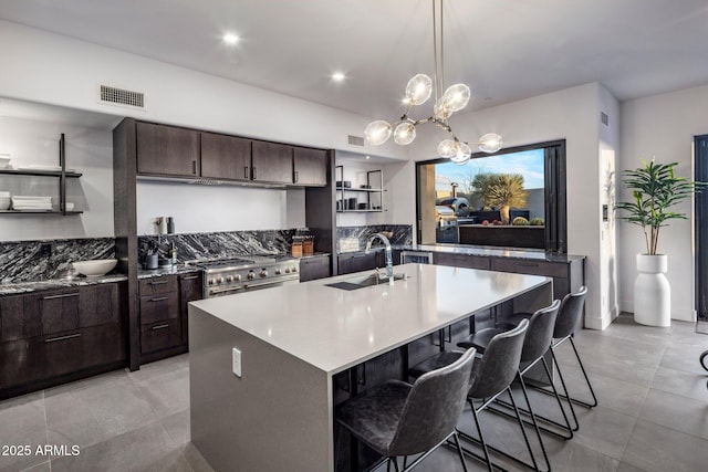 kitchen featuring visible vents, dark brown cabinetry, double oven range, a kitchen breakfast bar, and a sink