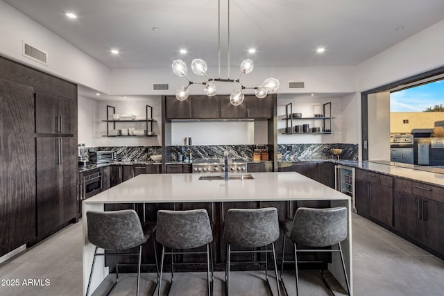 kitchen with visible vents, open shelves, a sink, a kitchen breakfast bar, and dark brown cabinets