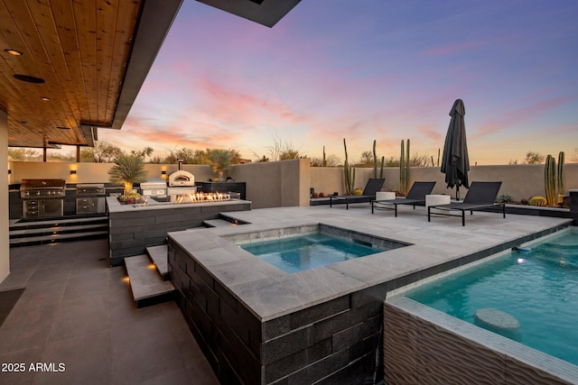 pool at dusk with a patio area, area for grilling, an outdoor kitchen, and fence