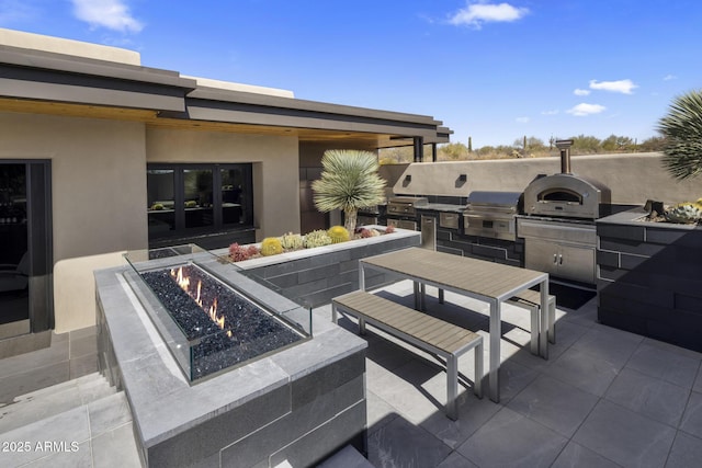 view of patio featuring outdoor dining space, exterior kitchen, grilling area, and an outdoor fire pit