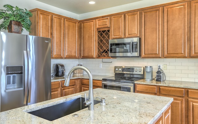 kitchen with light stone counters, decorative backsplash, appliances with stainless steel finishes, brown cabinetry, and a sink