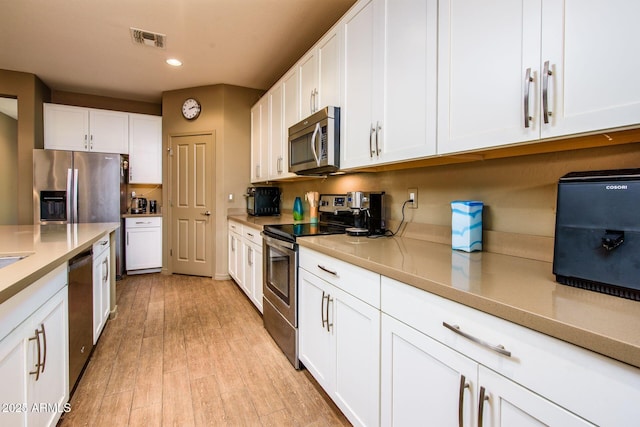 kitchen with light wood finished floors, visible vents, appliances with stainless steel finishes, light countertops, and white cabinetry