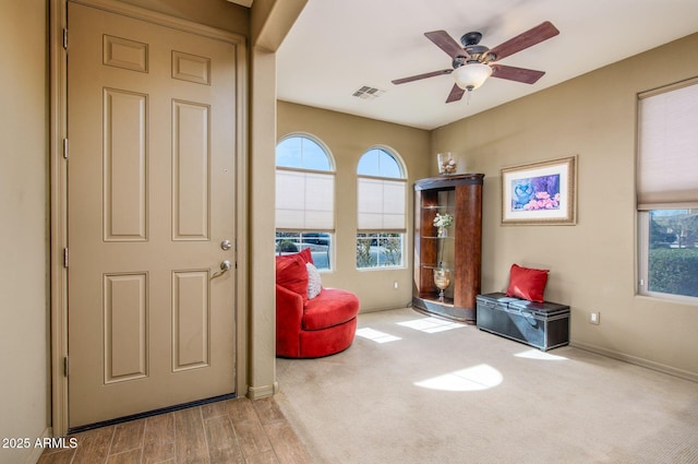 living area with baseboards, a ceiling fan, visible vents, and a healthy amount of sunlight