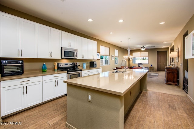 kitchen featuring a center island with sink, white cabinets, stainless steel appliances, light countertops, and a sink