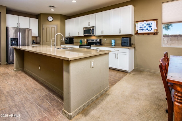 kitchen with a center island with sink, light countertops, appliances with stainless steel finishes, white cabinets, and a sink