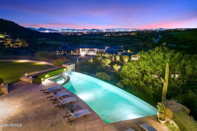 pool at dusk with an in ground hot tub and a patio area