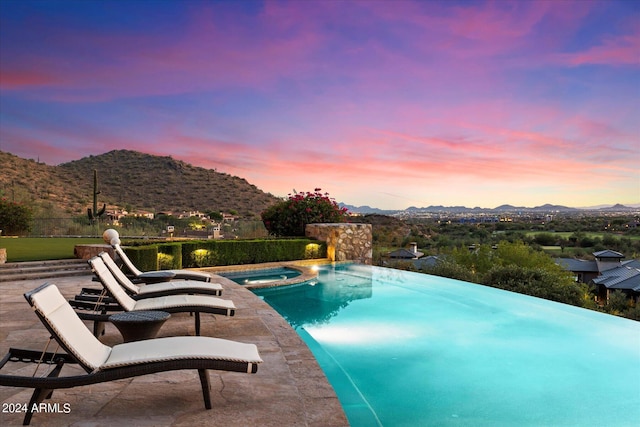 pool at dusk with a mountain view and an in ground hot tub