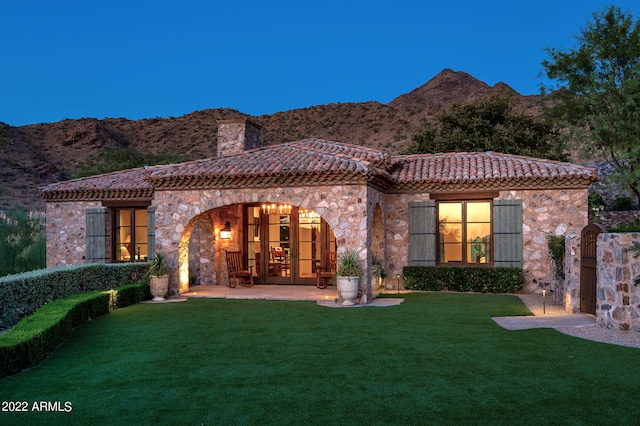 back house at twilight featuring a mountain view, a lawn, and a patio