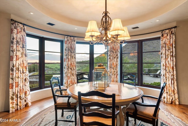 dining space featuring plenty of natural light, a raised ceiling, hardwood / wood-style floors, and a chandelier