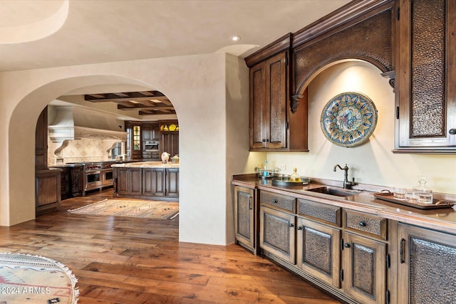 bar with custom range hood, hardwood / wood-style floors, sink, dark brown cabinets, and tasteful backsplash