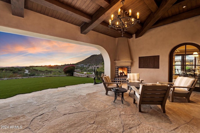 patio terrace at dusk featuring an outdoor living space with a fireplace, a lawn, and a mountain view