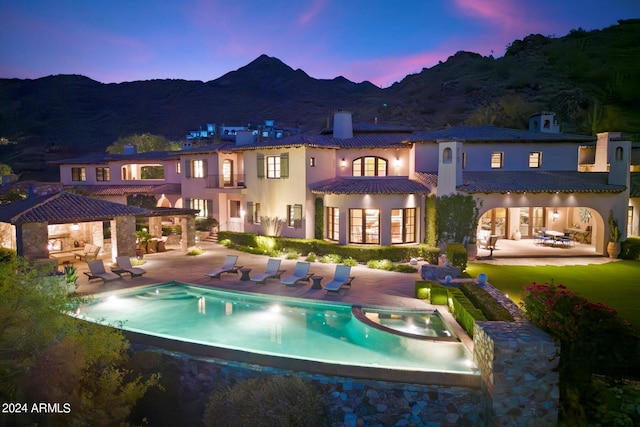 back house at dusk with a mountain view, a pool with hot tub, a patio, and a gazebo