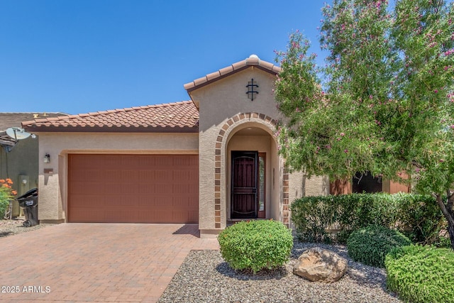 mediterranean / spanish-style house with stucco siding, an attached garage, a tile roof, and decorative driveway