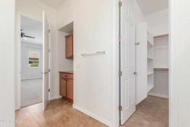 hall featuring light colored carpet, baseboards, and light tile patterned flooring