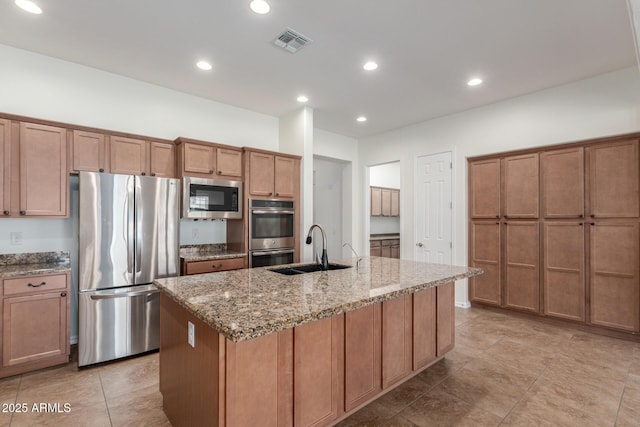kitchen featuring stainless steel appliances, a sink, a center island with sink, light stone counters, and recessed lighting