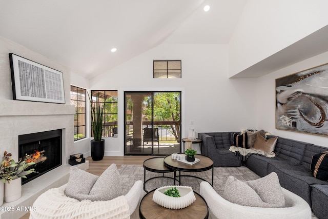 living area featuring recessed lighting, wood finished floors, a warm lit fireplace, and high vaulted ceiling