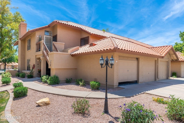 mediterranean / spanish-style house with a tiled roof, a chimney, an attached garage, and stucco siding