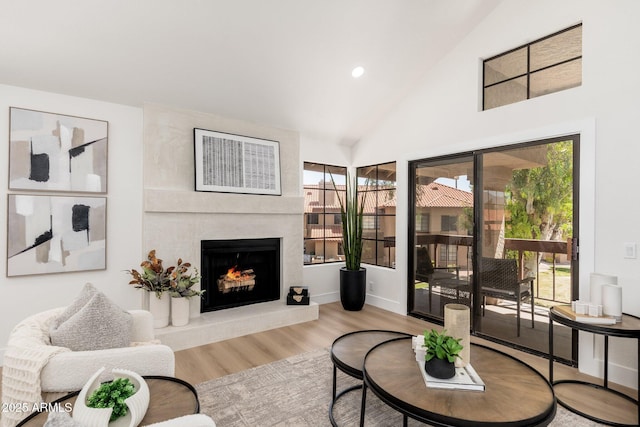 living room with wood finished floors, high vaulted ceiling, baseboards, a warm lit fireplace, and recessed lighting
