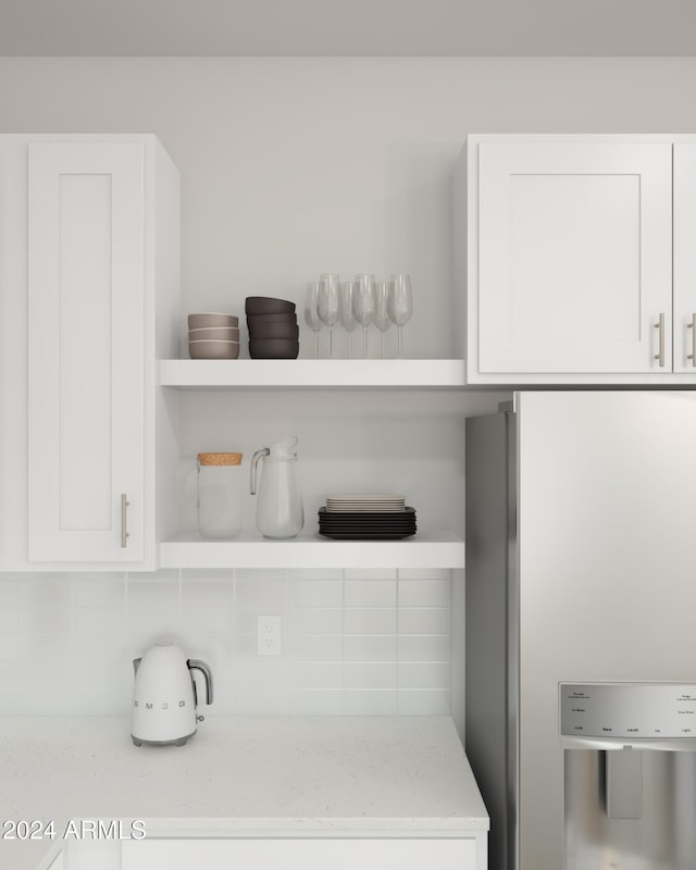 interior details featuring light stone counters, backsplash, white cabinetry, and stainless steel refrigerator