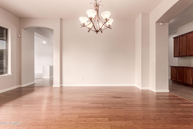 unfurnished dining area featuring arched walkways, baseboards, light wood-style flooring, and a chandelier