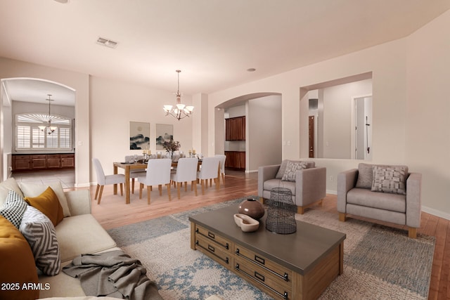 living room featuring arched walkways, an inviting chandelier, wood finished floors, and visible vents