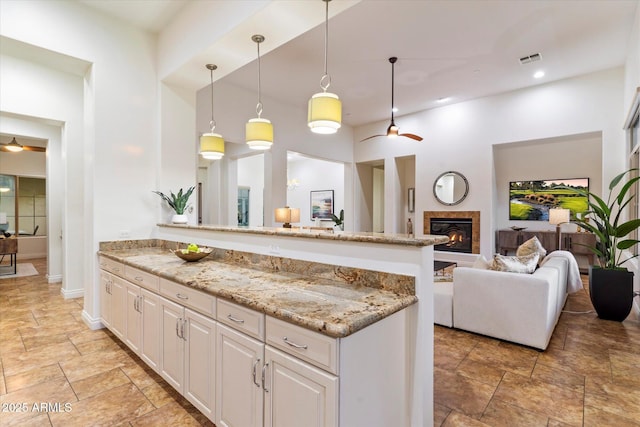 kitchen featuring ceiling fan, white cabinets, light stone counters, and decorative light fixtures