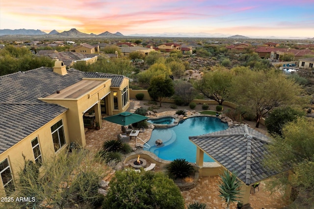 pool at dusk featuring a mountain view, a patio, and an in ground hot tub