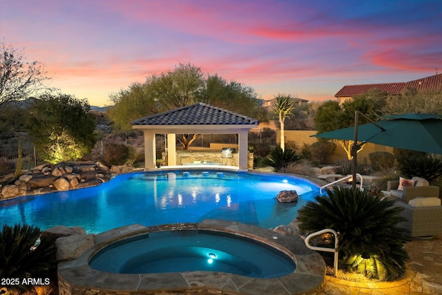 pool at dusk with a gazebo and an in ground hot tub