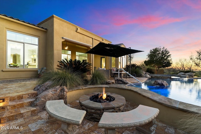 pool at dusk featuring a patio and a fire pit