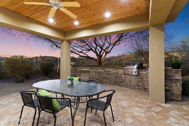 patio terrace at dusk featuring ceiling fan, an outdoor kitchen, and grilling area