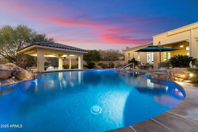 pool at dusk with pool water feature and a patio