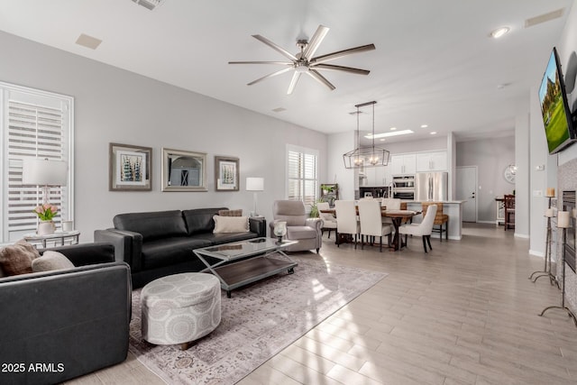 living room with ceiling fan with notable chandelier and light hardwood / wood-style flooring