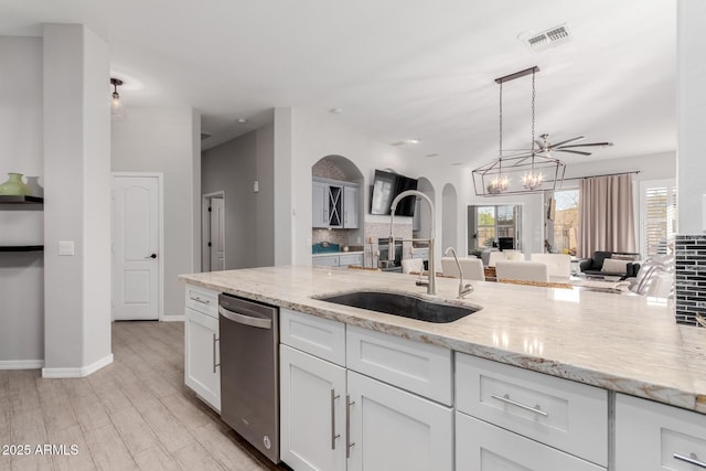 kitchen featuring sink, dishwasher, backsplash, light stone counters, and white cabinets