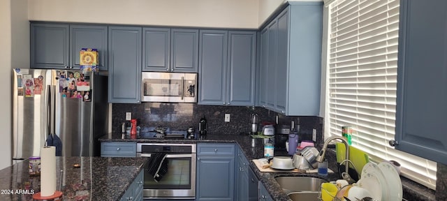 kitchen featuring appliances with stainless steel finishes, tasteful backsplash, blue cabinets, sink, and dark stone countertops