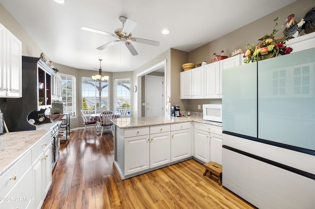 kitchen featuring white cabinetry, ceiling fan with notable chandelier, light wood finished floors, a peninsula, and white microwave