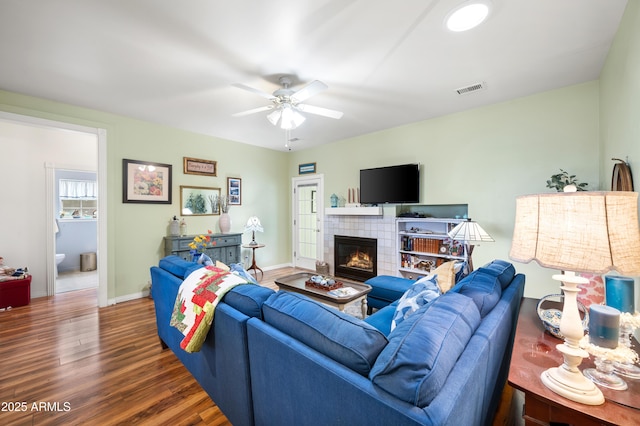 living room featuring visible vents, baseboards, ceiling fan, wood finished floors, and a tiled fireplace