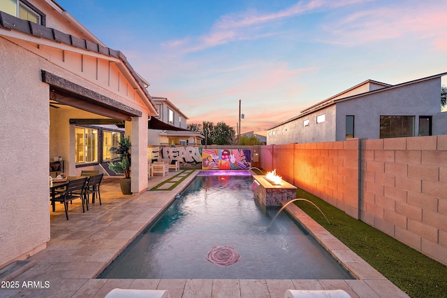 pool at dusk featuring pool water feature, a fire pit, and a patio