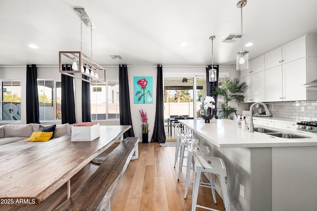 kitchen featuring backsplash, decorative light fixtures, light wood-type flooring, white cabinets, and sink