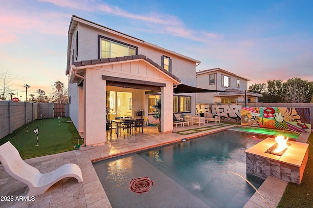 pool at dusk with a patio area and a fire pit