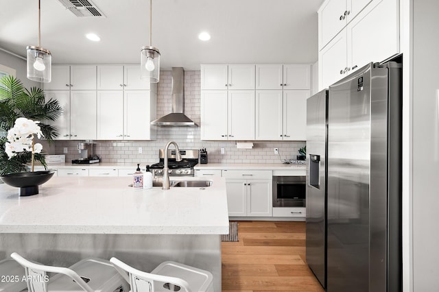 kitchen featuring hanging light fixtures, appliances with stainless steel finishes, wall chimney range hood, and white cabinetry