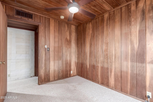 carpeted spare room with wooden ceiling, visible vents, ceiling fan, and wooden walls