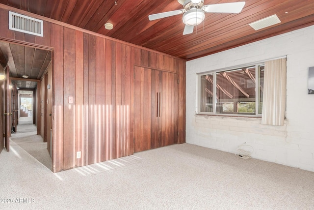 carpeted spare room featuring a ceiling fan, wood ceiling, visible vents, and wood walls